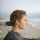 Profile portrait of a teenage girl looking out to sea from a beach at sunset.